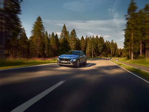 Pohled zepředu na Nový Hyundai Kona v barvě Surfy Blue, jedoucí po polní cestě lesem.